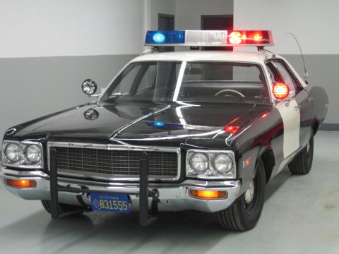 1991 Ford LTD Crown Victoria - black-and-white Dodge police car with quad headlights, push bar, and California plate 831555 sits in a garage.