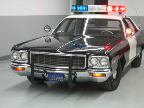 1991 Ford LTD Crown Victoria - black-and-white Dodge police car with chrome grille, push bumper, and California plate 831555 in a garage.