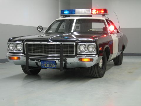 1991 Ford LTD Crown Victoria - Dodge police car in black and burgundy with a push bar and California plate 831555 sits under garage lighting.