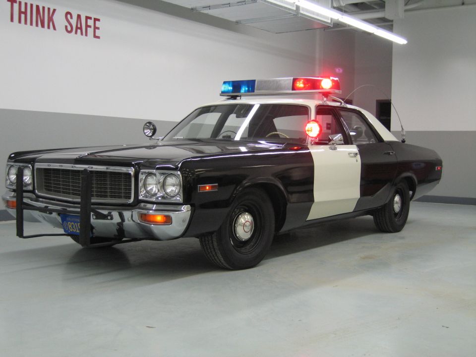 Front-three-quarter view of a black-and-white Dodge police car with push bumper in a garage
