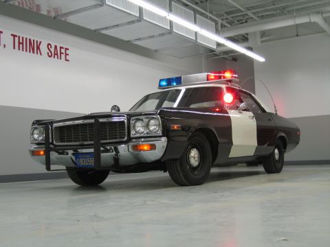 1991 Ford LTD Crown Victoria - low-angle view of a black-and-white Dodge police car with push bumper and California plate 831555 in a garage.