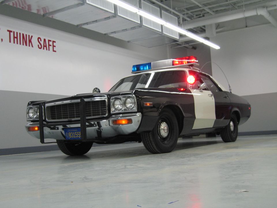 Low front view of a black-and-white Dodge police car with lit beacons and push bumper