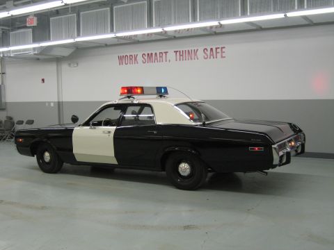 1991 Ford LTD Crown Victoria - black-and-white police sedan seen from the rear quarter with lit roof beacons inside a garage marked WORK SMART, THINK SAFE.