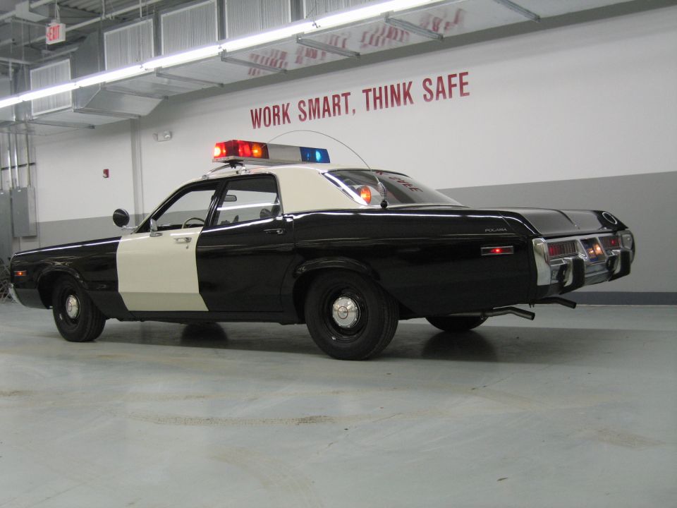 Rear-three-quarter view of a black-and-white police sedan with POLICE badge on rear fender