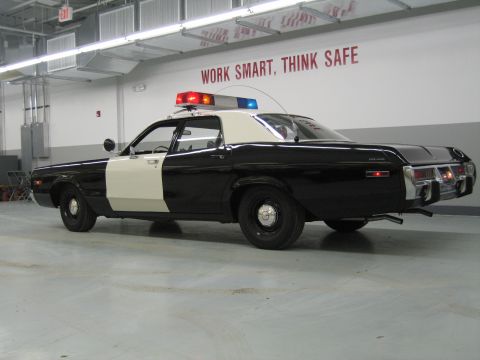 1991 Ford LTD Crown Victoria - black-and-white police sedan shown from the side rear with lit roof beacons and POLICE lettering on the fender.