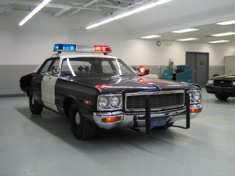 1991 Ford LTD Crown Victoria - black-and-white Dodge police car with chrome push bumper and California plate 831555 parked in an indoor shop.