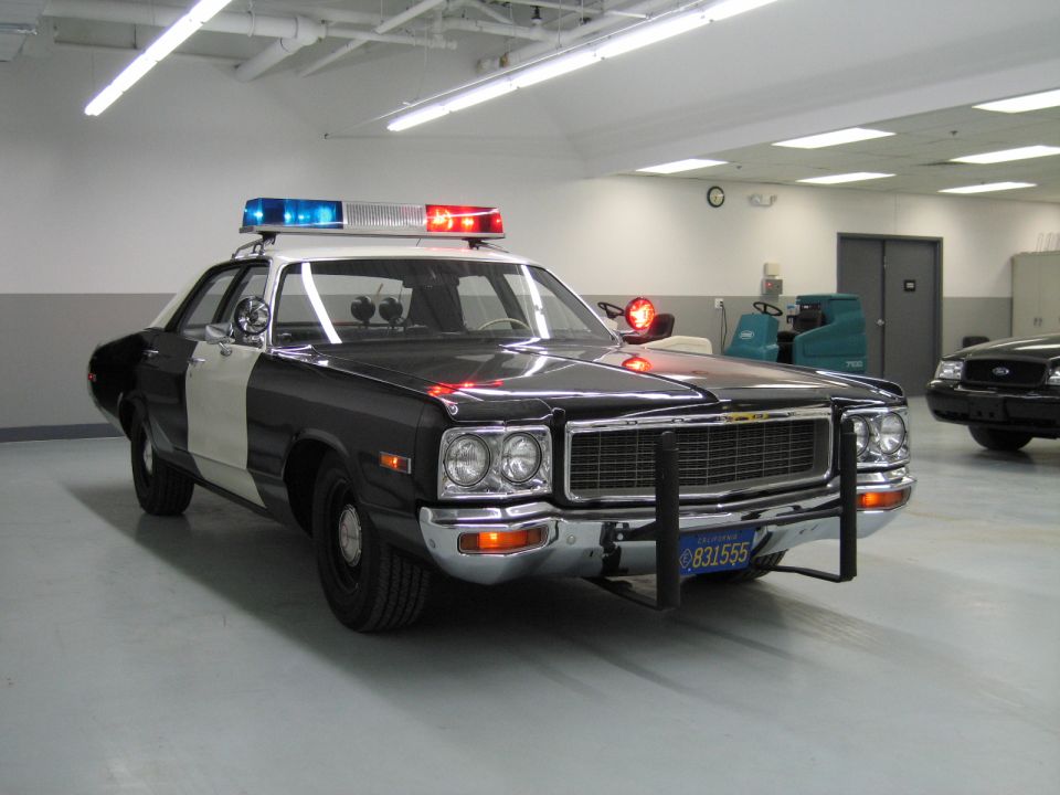 Black-and-white Dodge police car with push bumper and California plate 831555 in a shop