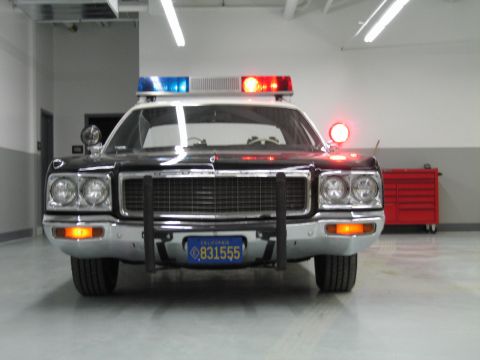 1991 Ford LTD Crown Victoria - head-on front view of a black-and-white Dodge police car with push bumper and California plate 831555 in a garage.