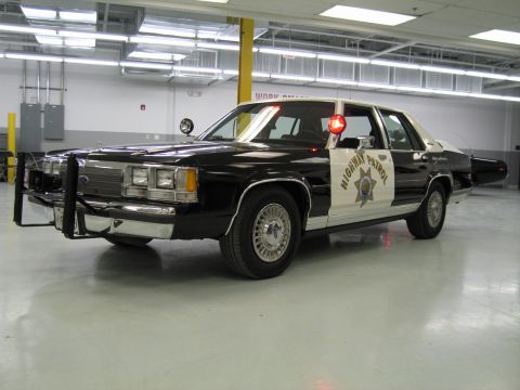 1991 Ford LTD Crown Victoria - black-and-white Ford California Highway Patrol sedan with push bumper and door star emblem in a garage.