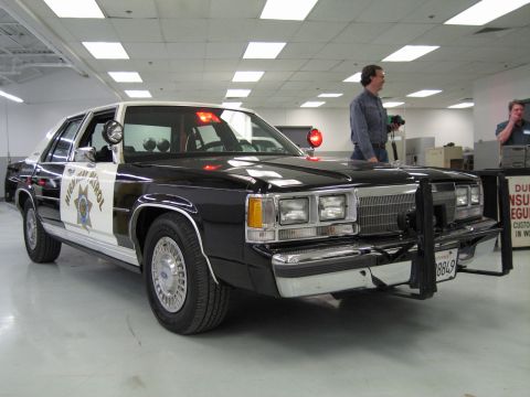 1991 Ford LTD Crown Victoria - black-and-white Ford California Highway Patrol cruiser with a chrome push bar and red roof beacons sits in a bright shop.