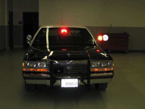 1991 Ford LTD Crown Victoria - Front view of a black-and-white Ford patrol car with illuminated headlights, push bar, and California plate 888849.