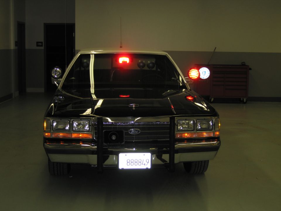 Front view of black-and-white Ford police car with lit emergency lights, plate 888849
