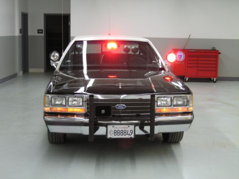 1991 Ford LTD Crown Victoria - Front of a black-and-white Ford police sedan with chrome push bar and lit lights, a red tool chest in the background.