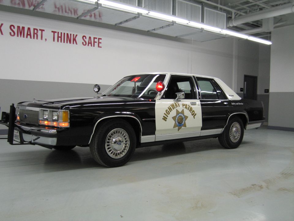 Side profile of black-and-white CHP Ford sedan, Work Smart Think Safe wall text