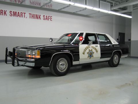 1991 Ford LTD Crown Victoria - Front three-quarter view of a black-and-white CHP Ford sedan with Highway Patrol gold-star decal and chrome push bar.