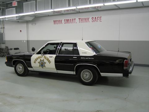1991 Ford LTD Crown Victoria - Driver-side rear three-quarter view of a black-and-white CHP Ford sedan parked in a clean shop.
