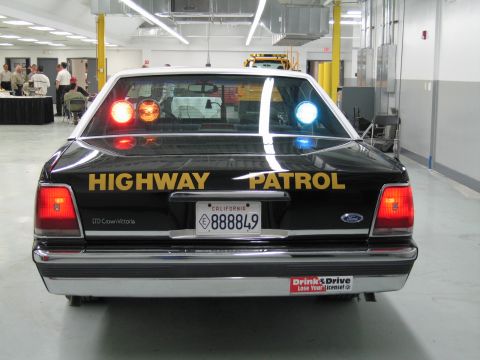 1991 Ford LTD Crown Victoria - Rear view of a black-and-white Ford LTD Crown Victoria CHP cruiser with Highway Patrol lettering and lit beacons.