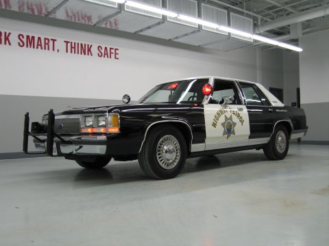 1991 Ford LTD Crown Victoria - Front three-quarter view of a black-and-white CHP Ford sedan with chrome push bar, A-pillar spotlight, and gold star decal.