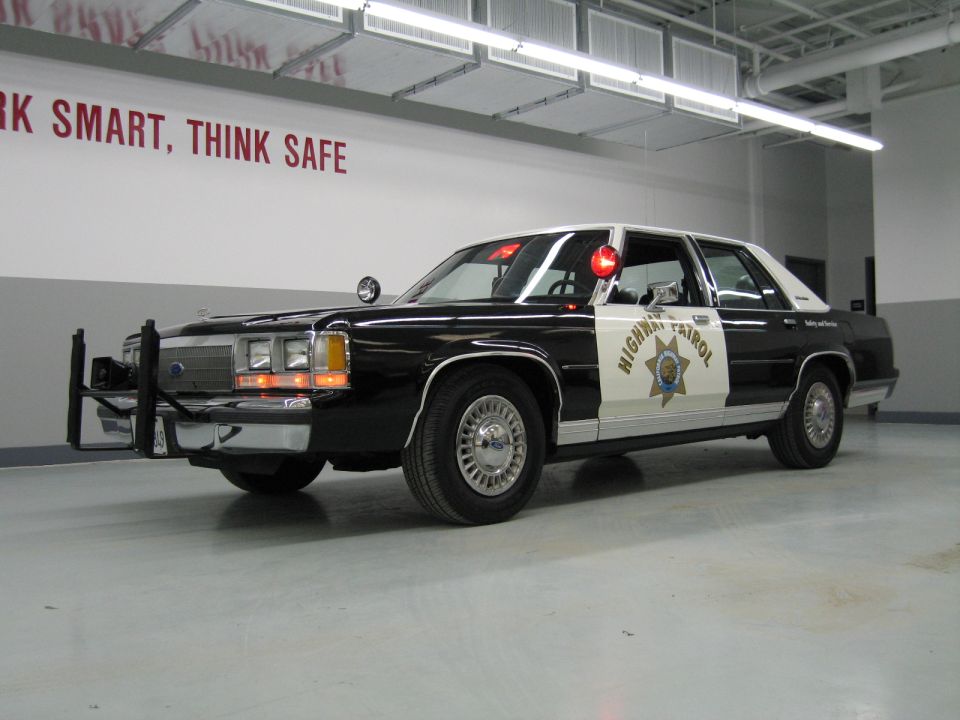 Front-quarter black-and-white CHP Ford sedan with push bar and spotlight