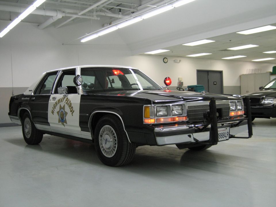 Front-quarter black-and-white CHP Ford sedan with push bar, second car behind