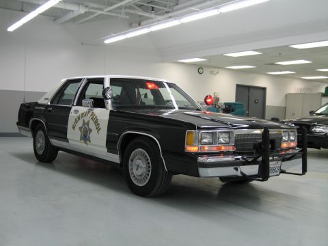 1991 Ford LTD Crown Victoria - Front three-quarter view of a black-and-white CHP Ford sedan with push bar and spotlight in a brightly lit garage.