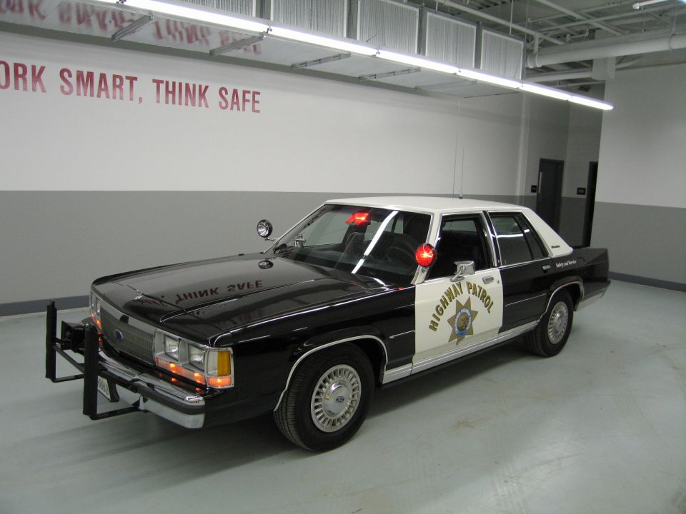 California Highway Patrol black and white Ford sedan parked under a 'Work Smart, Think Safe' sign