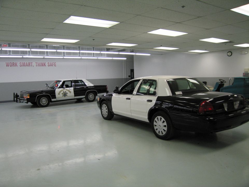 Two black and white police cars parked in a shop, an older sedan and a newer Crown Victoria