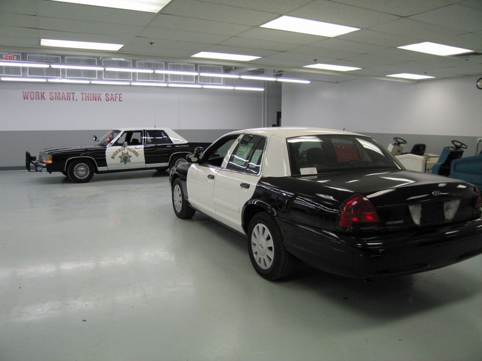 Rear three-quarter view of a black and white police sedan beside an older CHP cruiser