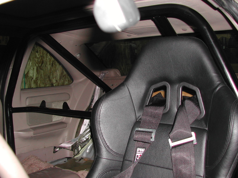Interior view of a racing seat with a roll cage and racing harness. Text on harness reads PRO 2000