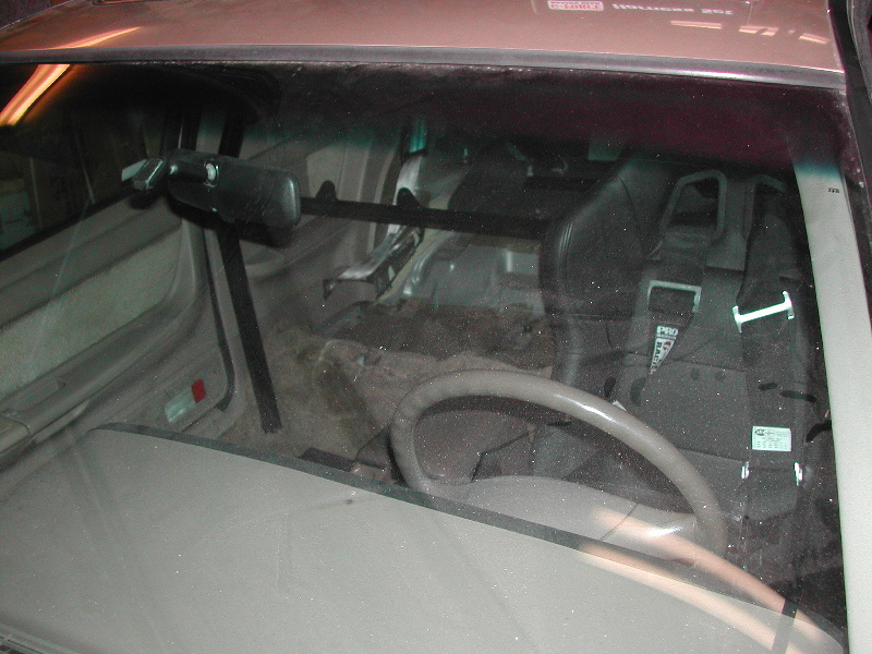 Interior shot of a car with a racing seat and harness, roll bar, and aftermarket steering wheel