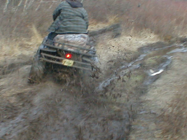 Rear view of ATV quad splashing through mud with rider in striped jacket