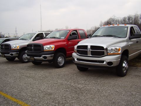 1997 Ford Taurus - Three Dodge Ram pickup trucks are lined up in a parking lot under an overcast sky.