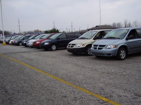 1997 Ford Taurus - Multiple minivans are parked in a lot under an overcast sky.