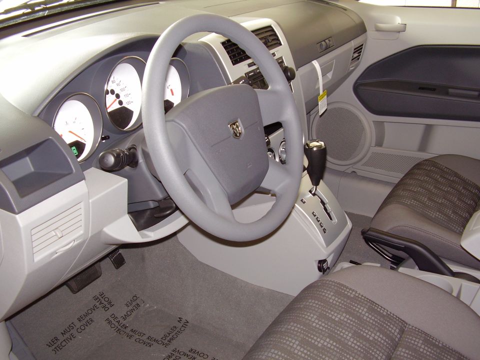 Car interior with steering wheel, dashboard gauges, gear shifter, and seats. Dodge logo on steering wheel