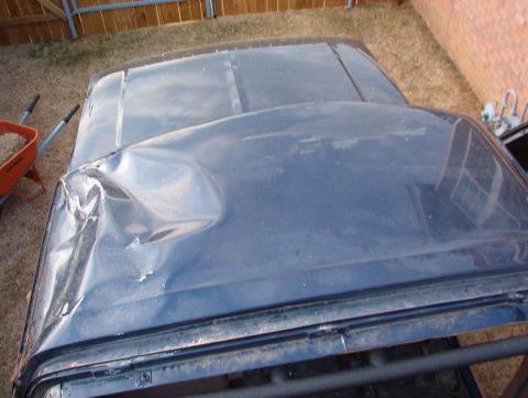 1994 Ford Bronco - The roof panel of a vehicle shows significant damage, with a large dent on the upper surface.