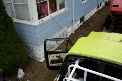 1978 Ford Bronco - A yellow truck cab sits next to a house, with a red vehicle on a trailer behind it.