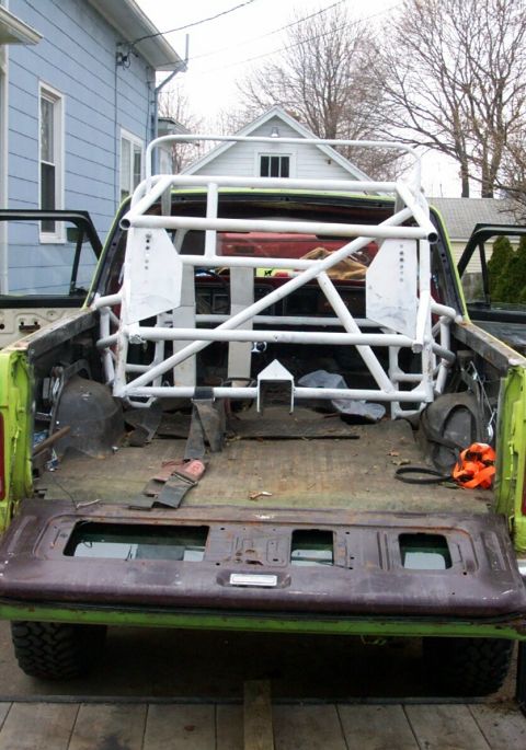 1978 Ford Bronco - The interior of a pickup truck bed is shown with a custom roll cage and various parts scattered around.