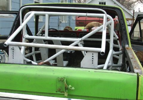 1978 Ford Bronco - Custom white rollcage installed in the bed of a green pickup truck, with a view of the interior and dashboard.