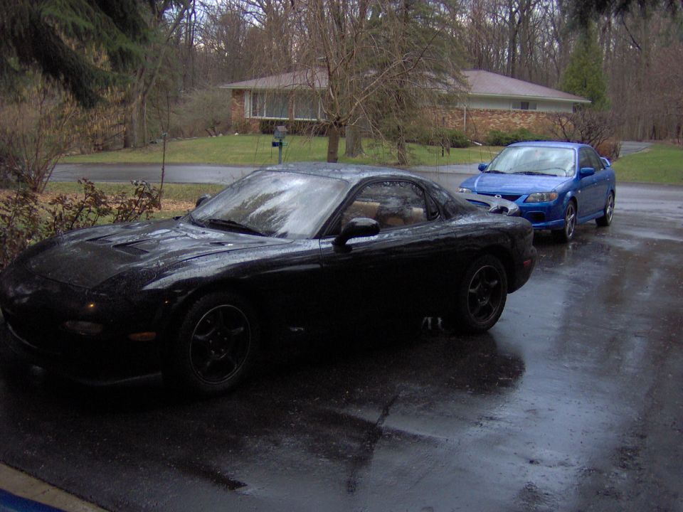 Wet black Mazda RX-7 coupe on driveway, front 3/4 view