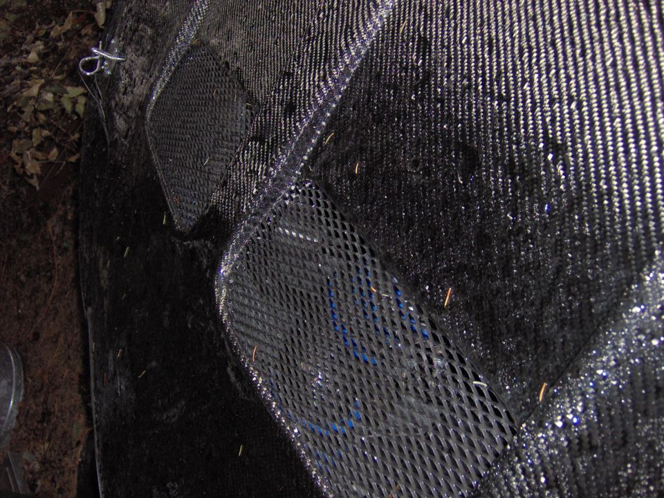 close-up of black car hood with diamond mesh vents, some water droplets visible