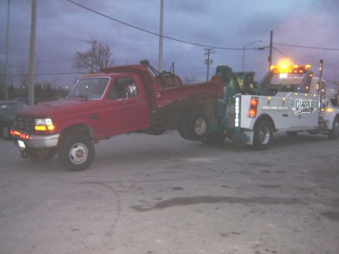 1992 Ford Bronco - A red dump truck is being towed by a white Cooper tow truck under an overcast sky.