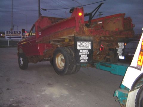 1992 Ford Bronco - A red dump truck with significant rust is being towed on a trailer.