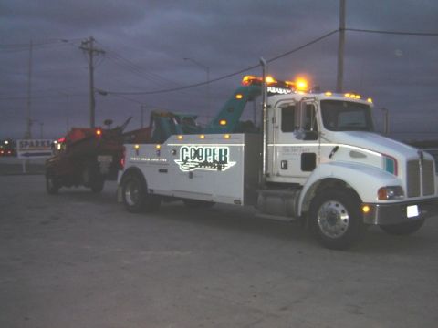 1992 Ford Bronco - A white tow truck is seen towing a dark SUV under a cloudy sky at dusk.