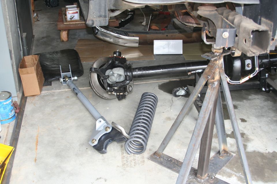 Solid front axle, coil spring, and radius arm on garage floor under a vehicle on steel jack stands