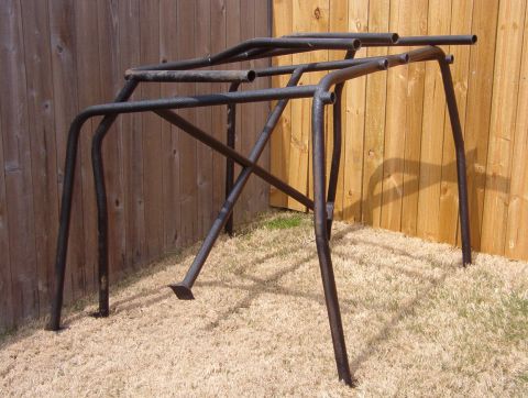 1994 Ford Bronco - A metal roll cage structure is shown outdoors, resting on dry grass in front of a weathered wooden fence.
