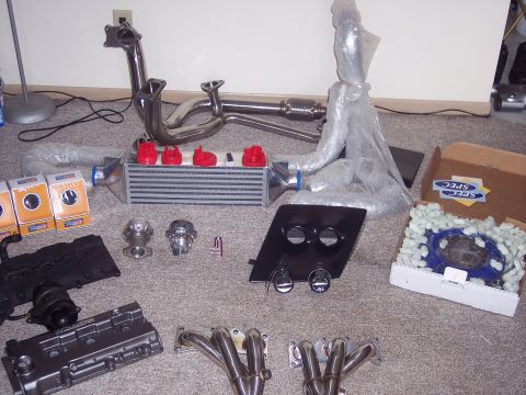 1995 Ford Probe - Collection of aftermarket car parts laid out on a carpeted floor.