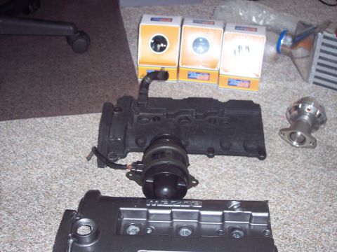 1995 Ford Probe - Various automotive engine parts, including a Mazda valve cover, are laid out on a carpeted floor.