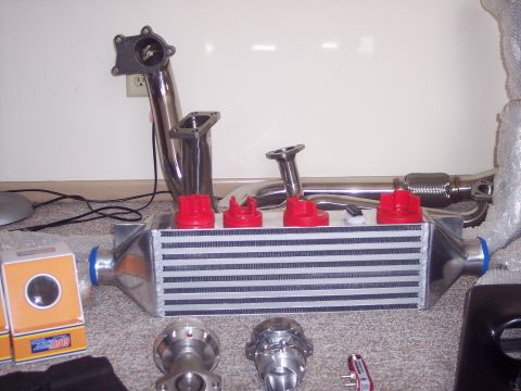 1995 Ford Probe - Various engine performance parts including an intercooler, exhaust piping, and blow-off valves are laid out on the floor.