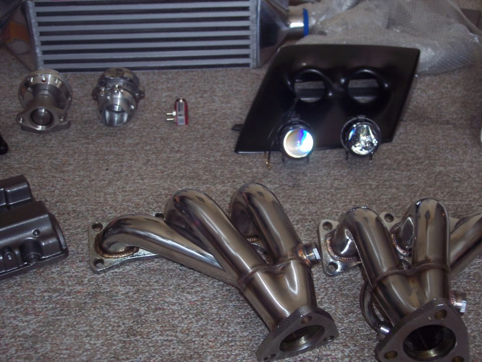 Performance exhaust manifold, blow-off valve, and intercooler laid out on carpet