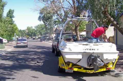1991 Ford Bronco - A boat on a trailer is being towed down a residential street by a truck, with a person attending to the boat.